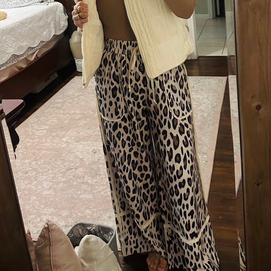 Person wearing a beige vest and leopard print pants in a bedroom.