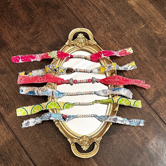 Handmade fabric word bracelets arranged on a decorative mirror on a wooden surface