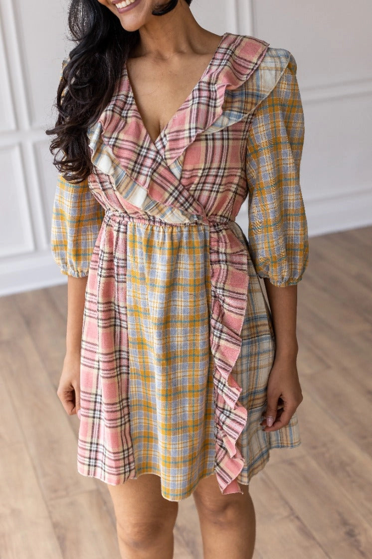 Plaid Ruffle Wrap Dress. Featuring a mix of soft plaid patterns, a flattering wrap design, and ruffled details along the neckline and hem.