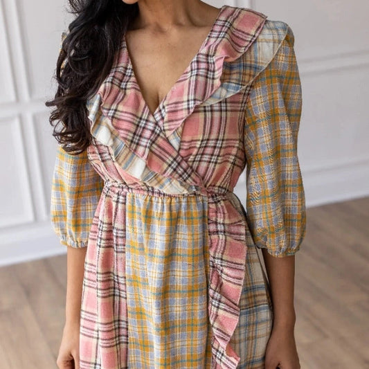 Plaid Ruffle Wrap Dress. Featuring a mix of soft plaid patterns, a flattering wrap design, and ruffled details along the neckline and hem.