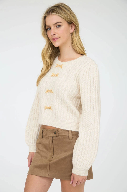 Cream Velvet Bow Cable Knit Sweater is a cozy and stylish addition to your wardrobe. Featuring a classic cable knit pattern and a round crew neckline.