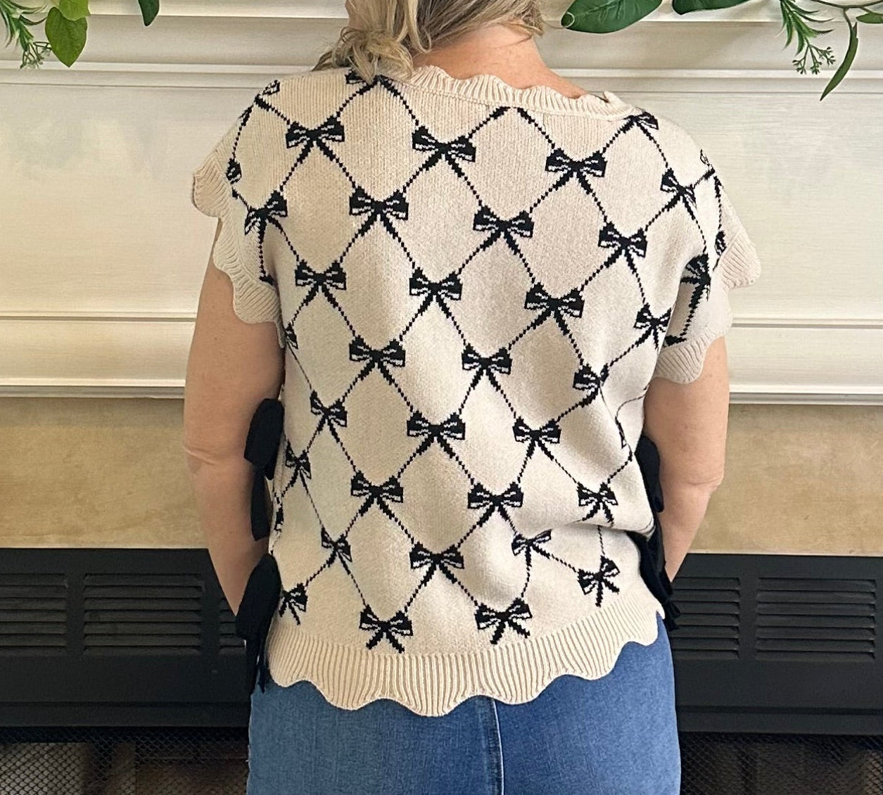 Person wearing a white sweater with black bow pattern in front of a fireplace.