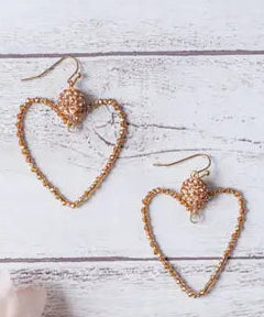 Heart-shaped earrings on a light wooden surface with a soft pink flower.