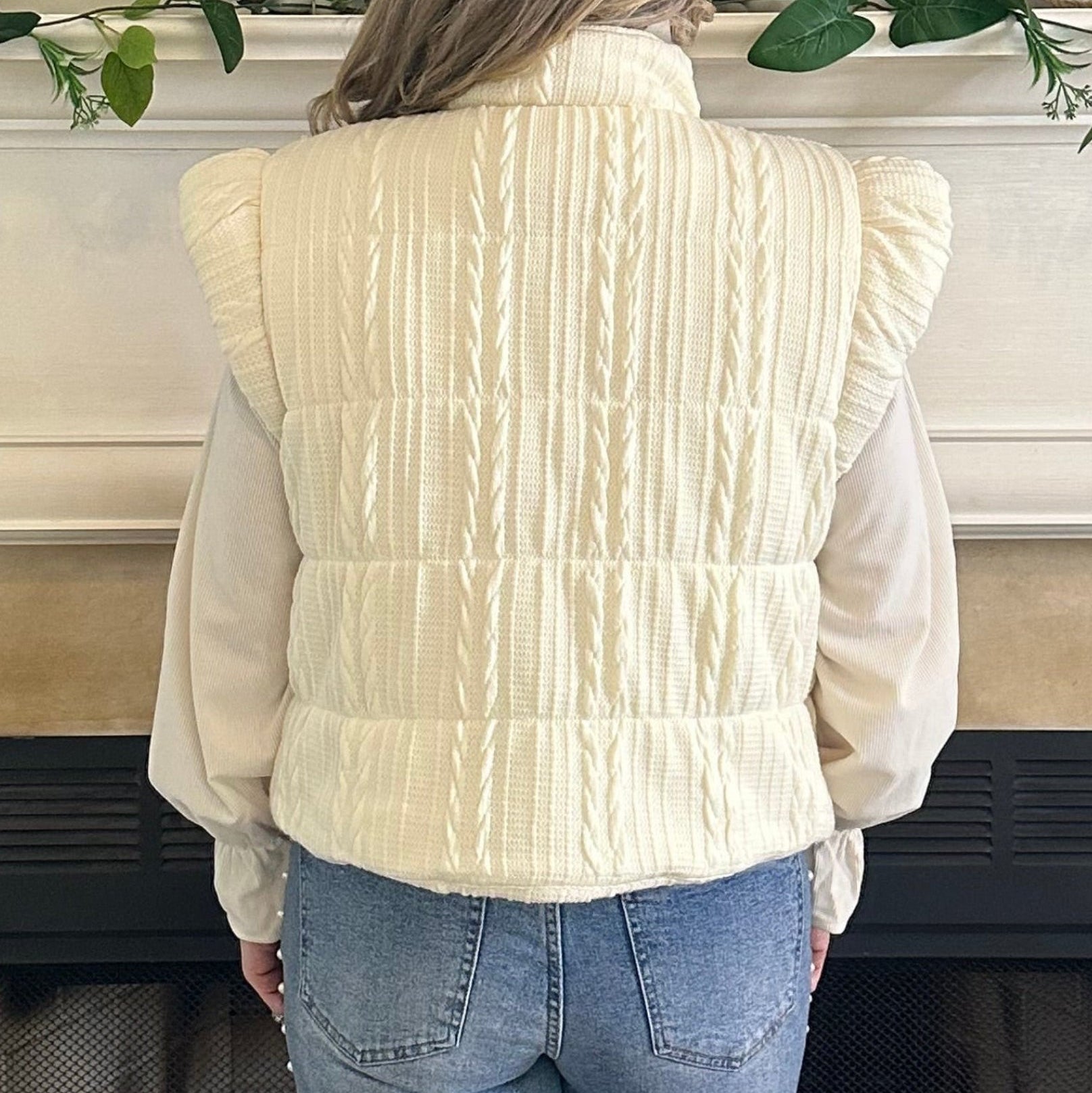 Person wearing a white sweater and blue jeans standing in front of a fireplace.