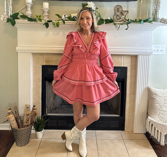 Woman in a pink dress standing in front of a fireplace with decorative items.