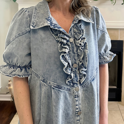 Person wearing a denim dress with ruffled collar and sleeves indoors.
