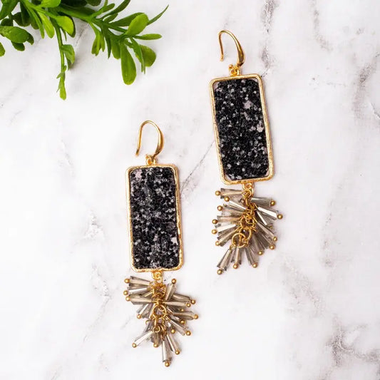 Gold and black earrings on a marble surface with green leaves.