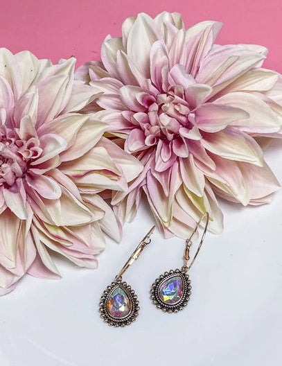Pair of earrings on a white plate with pink flowers against a pink background