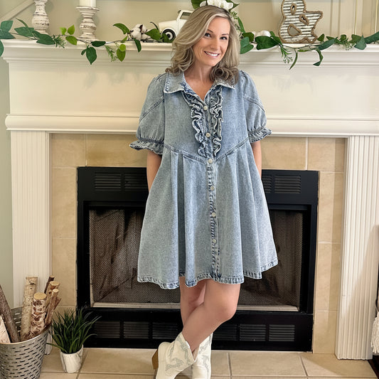 Woman in a denim dress standing in front of a fireplace with decorative elements.