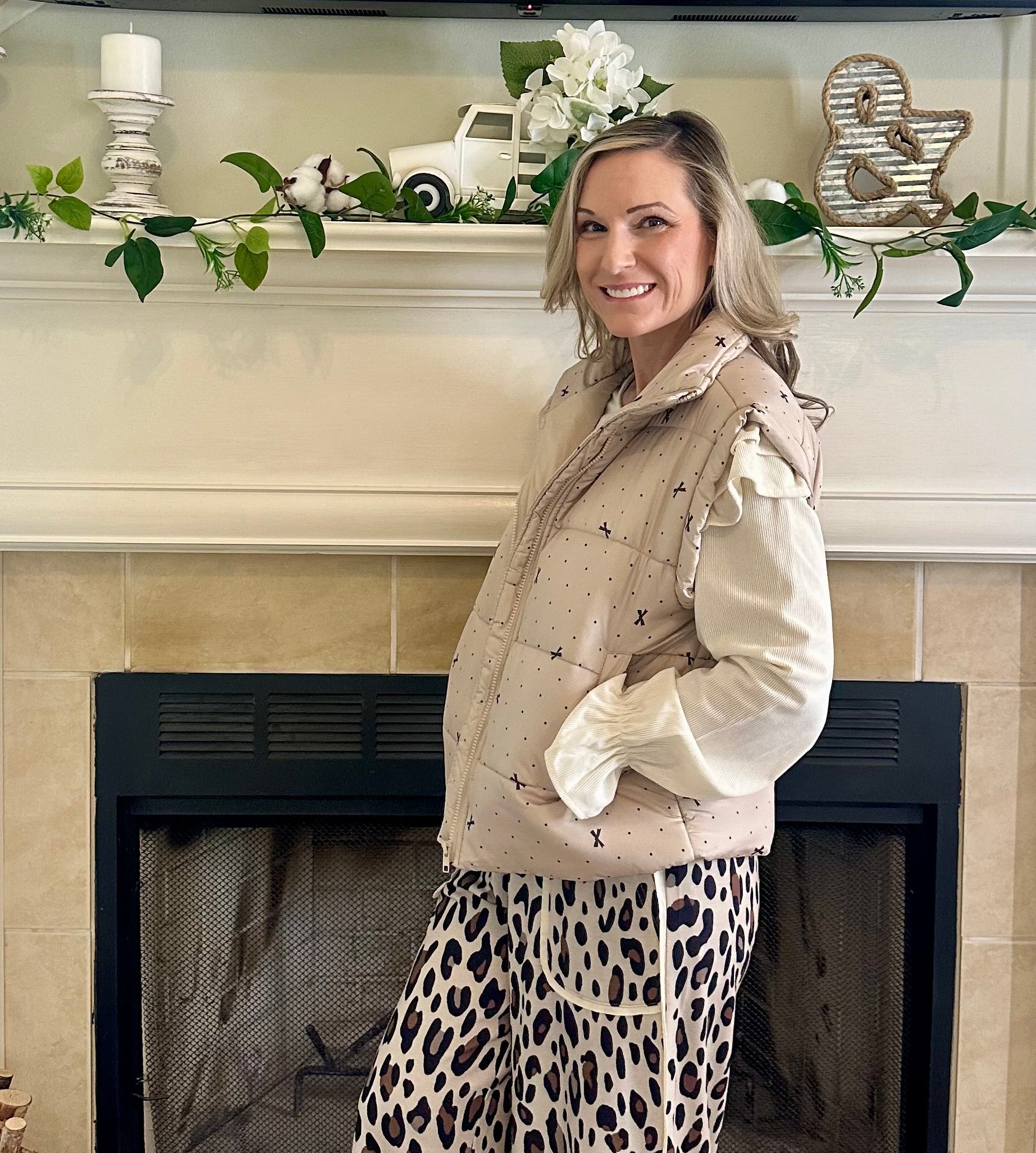 Woman standing in a living room with a fireplace and decorative mantel.