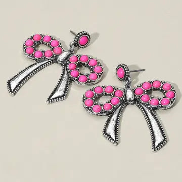 Bow-shaped earrings with pink stones on a beige background