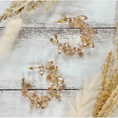 Pair of gold leaf earrings on a wooden surface with dried plants.