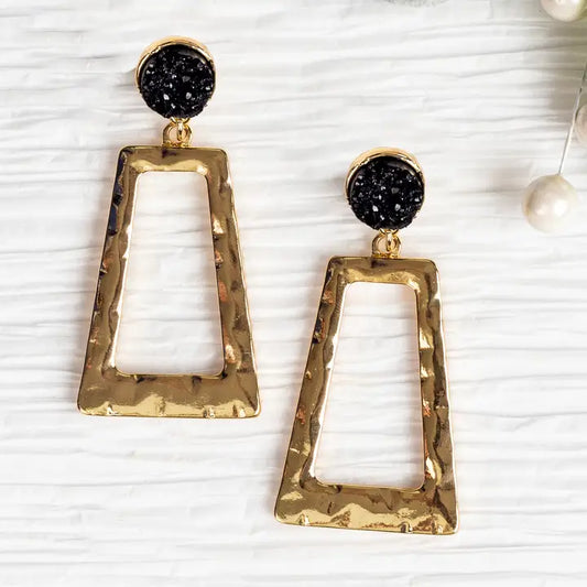 Pair of earrings with gold frames, white centers, and black drusy stones on a textured white background.