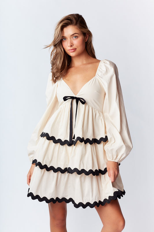 Ric-Rac Mini Dress is a playful and feminine piece that exudes effortless charm. Featuring a deep V-neck with a ribbon tie closure.