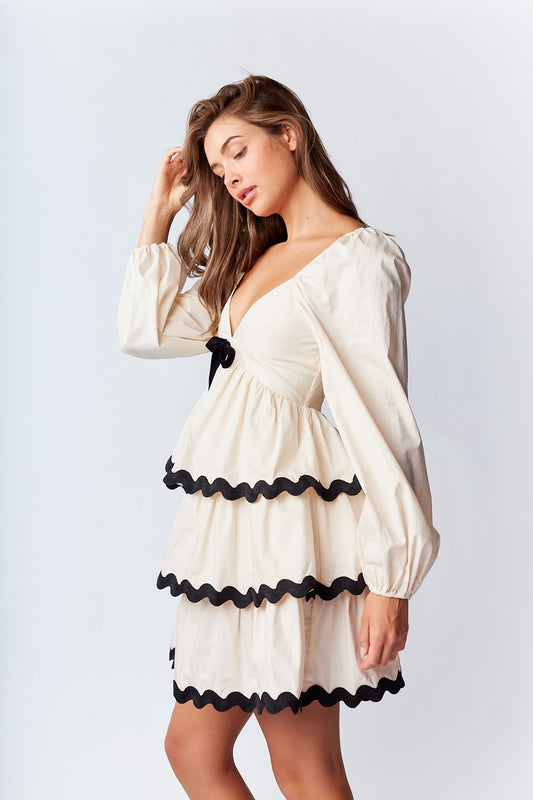 Ric-Rac Mini Dress is a playful and feminine piece that exudes effortless charm. Featuring a deep V-neck with a ribbon tie closure.