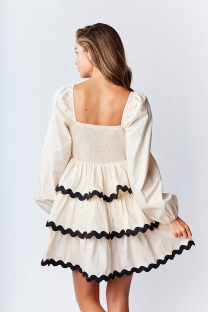 Ric-Rac Mini Dress is a playful and feminine piece that exudes effortless charm. Featuring a deep V-neck with a ribbon tie closure.