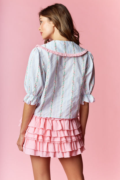  Sailor-Collar Cropped Blouse blends vintage charm with playful femininity. Designed with a relaxed fit and cropped length, this blouse features a sailor-style collar adorned with ruffle trim and delicate floral embroidery on a striped fabric. 