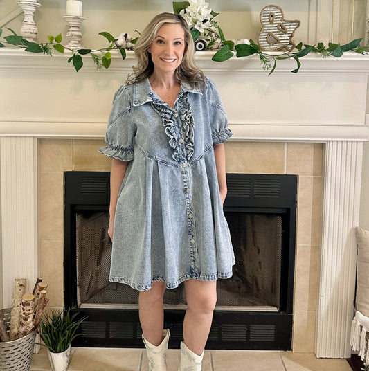 Woman wearing a denim dress with white boots standing in front of a fireplace.