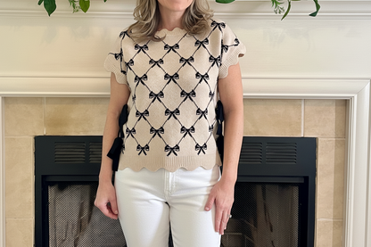 Woman wearing a beige sweater with black bow pattern in front of a fireplace.