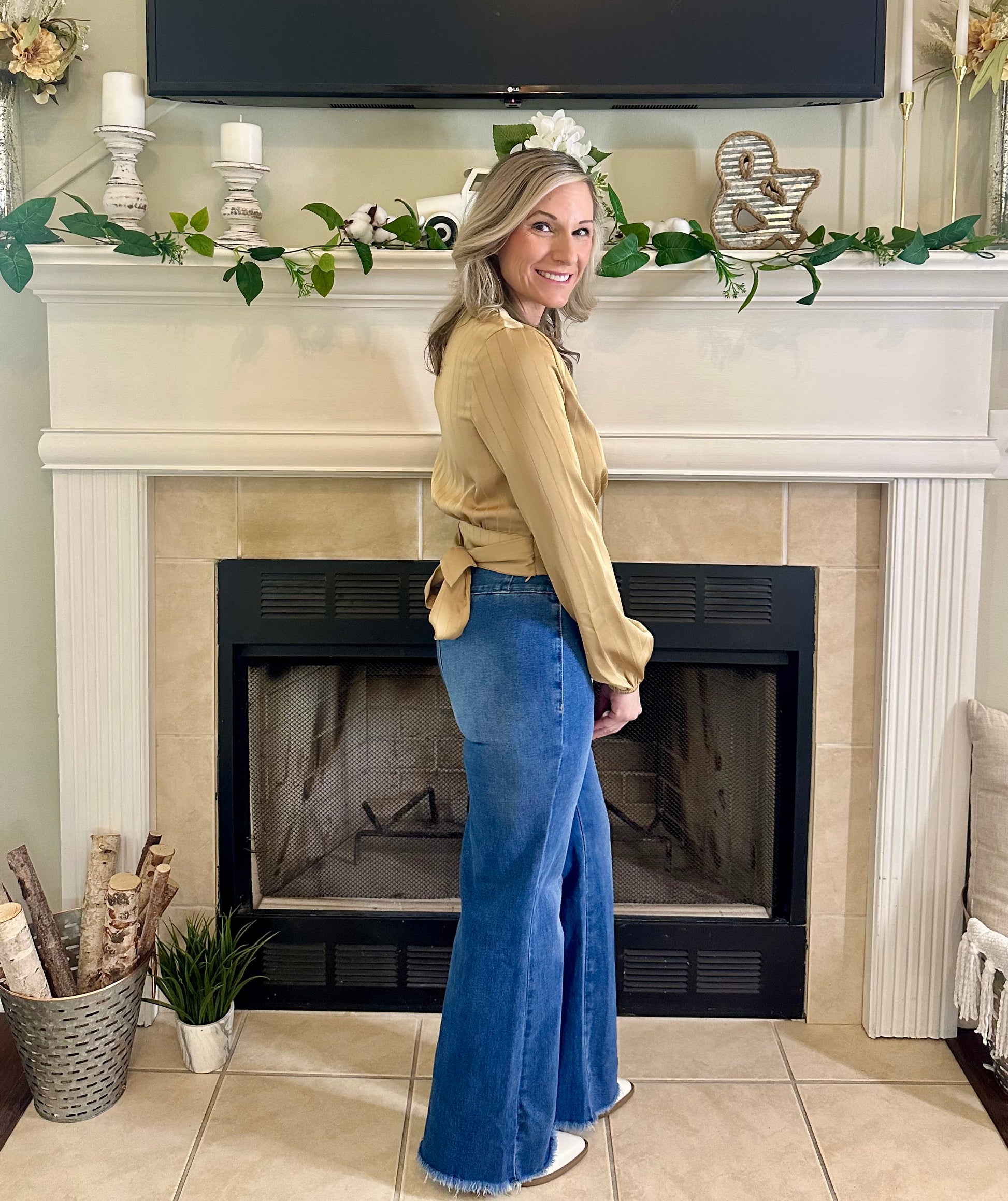 Woman standing in front of a fireplace wearing a yellow top and blue jeans.