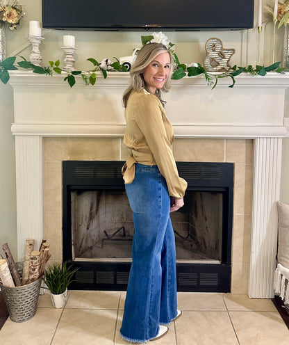 Woman standing in front of a fireplace wearing a yellow top and blue jeans.