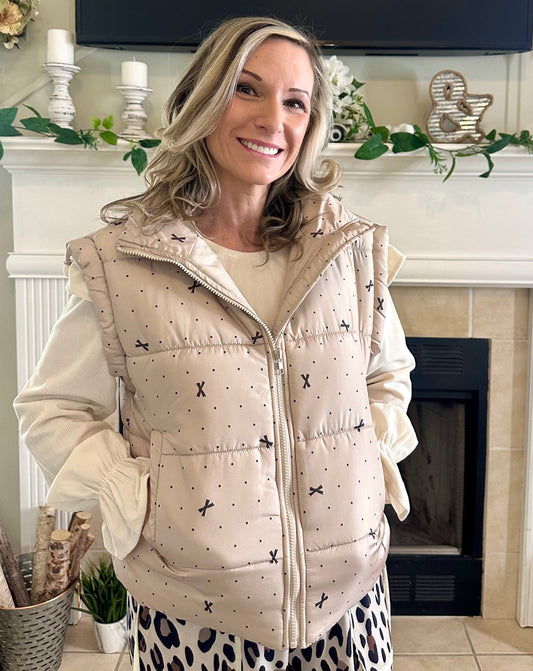 Woman wearing a beige puffer vest with black patterns in a home setting.