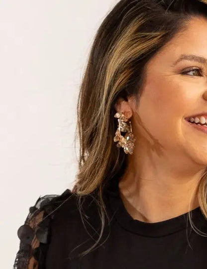Woman wearing a black top with a plain background and hoop earrings with champange color. 