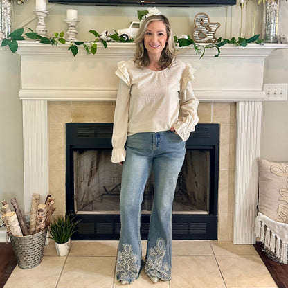 Woman in a white blouse and blue jeans standing in front of a fireplace.