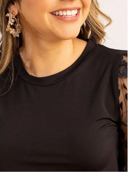 Close-up of a person wearing gold hoop earrings with champange color jewels and a  black background top with a blurred