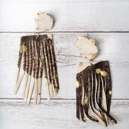 Pair of earrings with long, thin, layered design on a light wooden surface