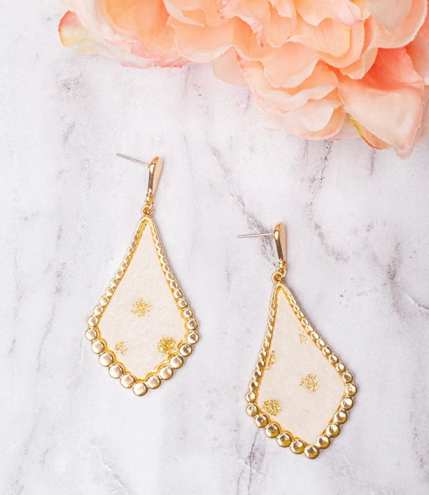Teardrop-shaped earrings with gold detailing on a marble surface with a pink flower.