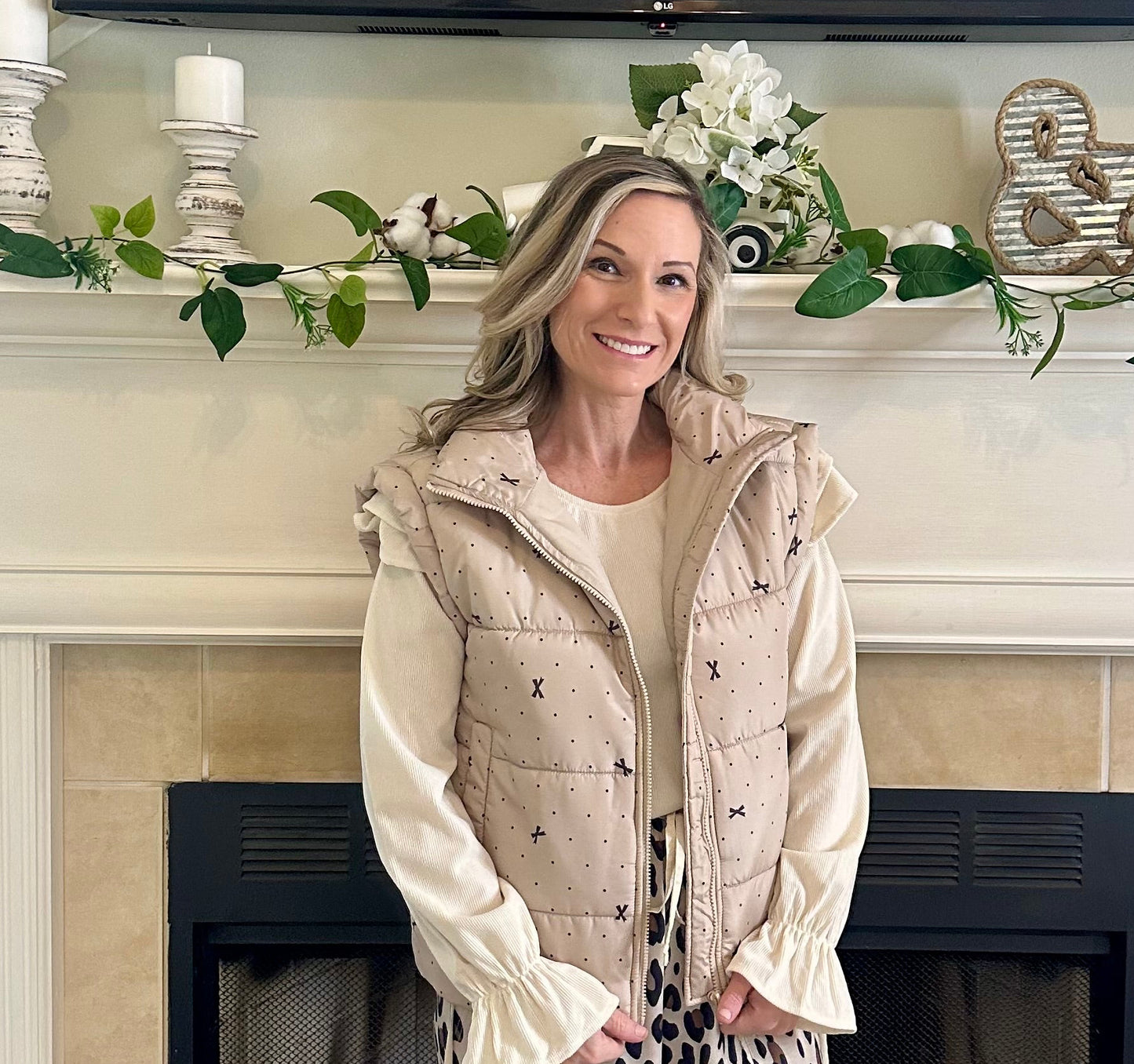 Woman standing in a living room with a fireplace and decorative items.