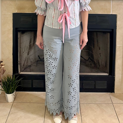 Person wearing a floral blouse and light blue pants standing in front of a fireplace.