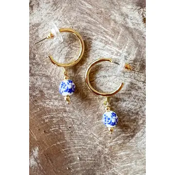 Gold hoop earrings with blue beads on a textured surface