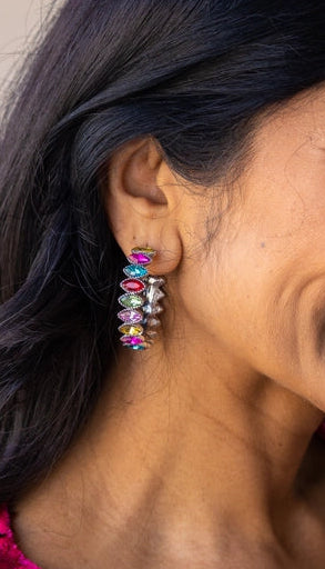Woman wearing colorful earrings with a pink sequined top against a neutral background