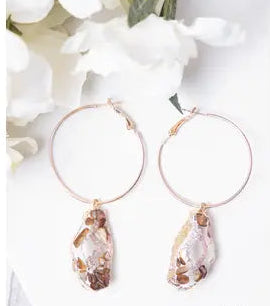 Gold hoop earrings with teardrop-shaped crystals on a white background with floral elements.