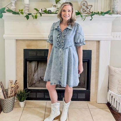 Woman in a denim dress standing in front of a fireplace