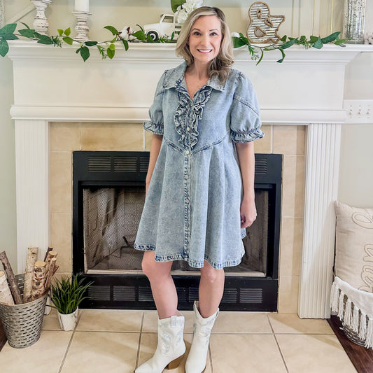 Woman in a denim dress standing in front of a fireplace