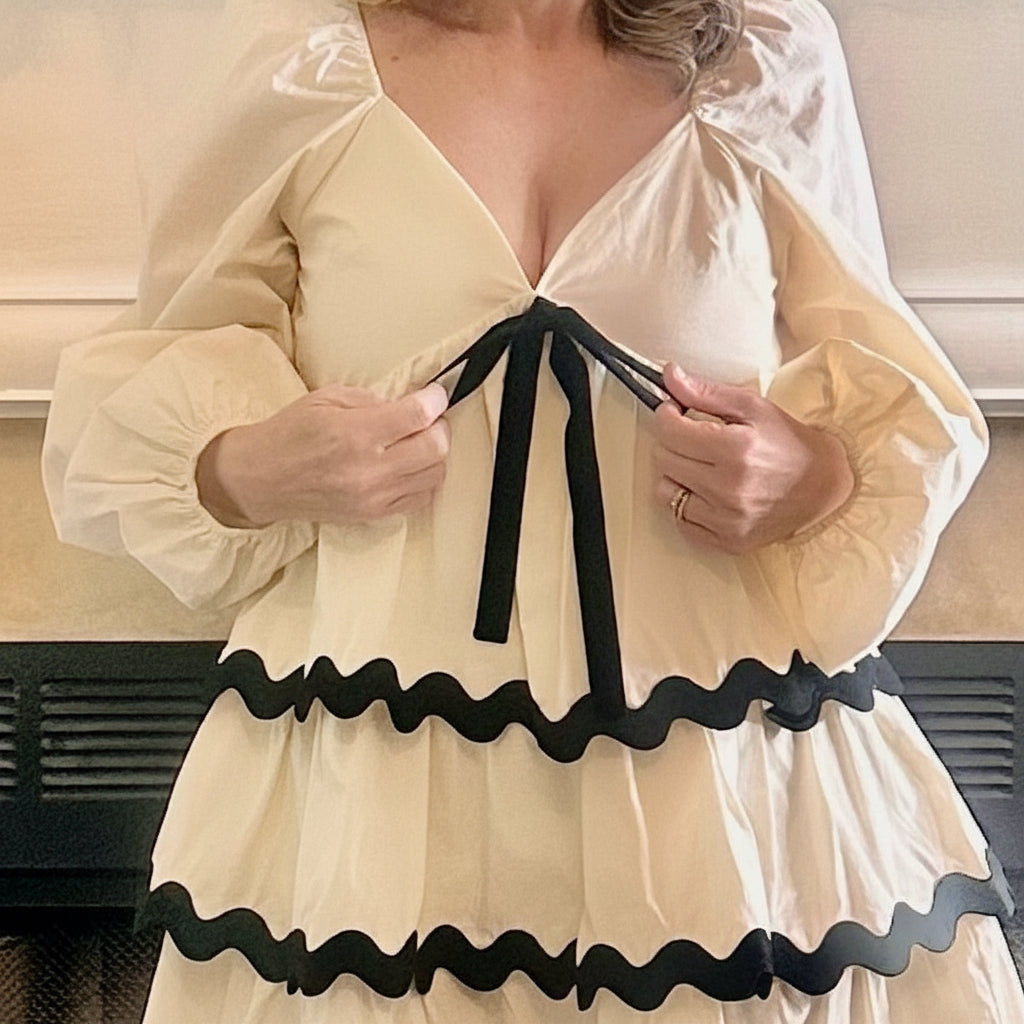 Woman wearing a beige dress with black trim, standing indoors.