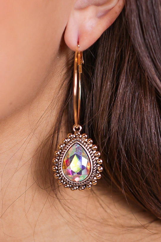 Close-up of a person wearing a rose gold earring with a colorful gemstone.