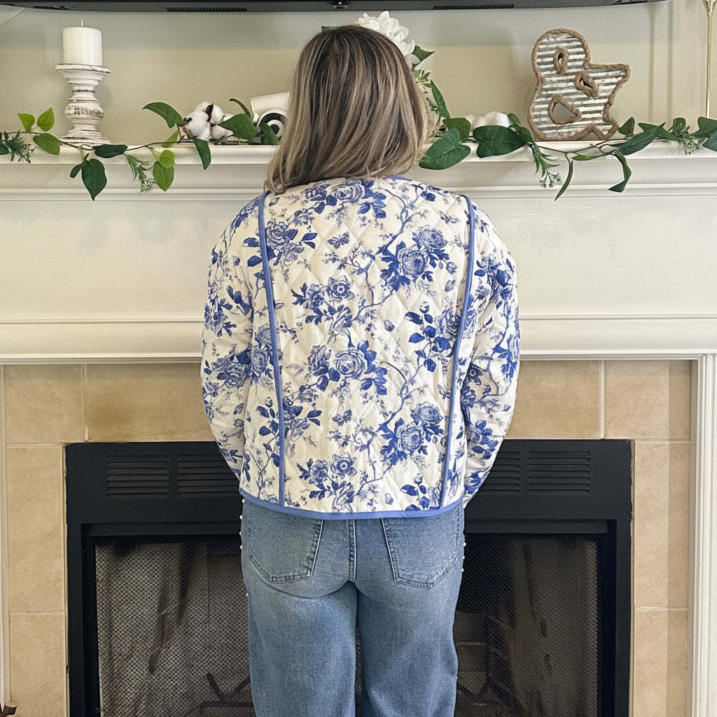 Person wearing a floral hoodie and jeans standing in front of a fireplace.