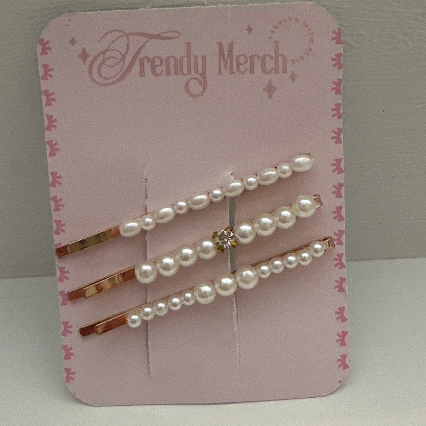Three pearl-barrel hair pins with rose gold metal and a small rhinestone accent, displayed on a pink 'Trendy Merch' backing card against a neutral gray background.