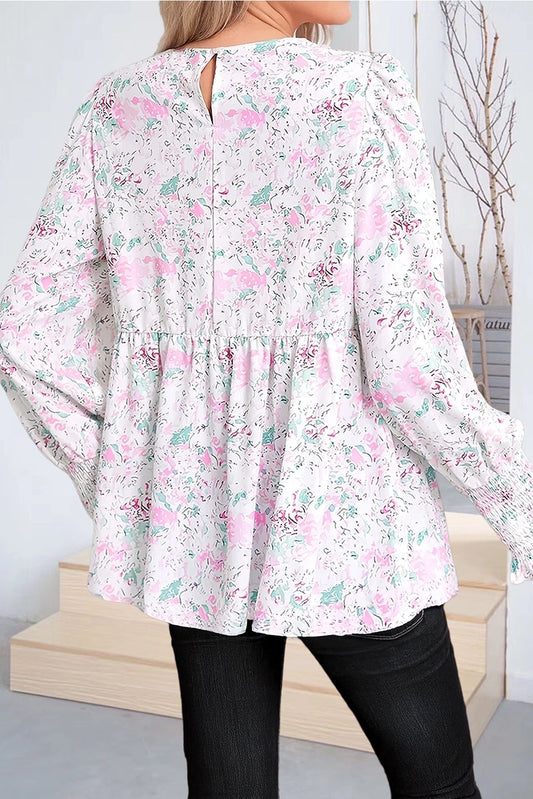 Floral Print Blouse. This blouse features a charming floral print in soft, pastel tones. The design includes a flattering V-neckline, long puffed sleeves with smocked cuffs, and a relaxed, flowy fit.