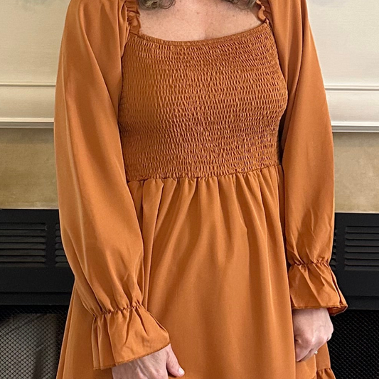 Person wearing a mustard yellow dress with long sleeves in an indoor setting.