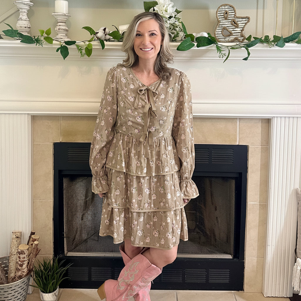 Woman in a floral dress and pink boots standing in front of a fireplace.