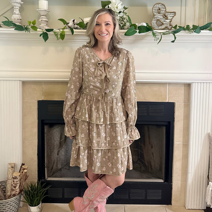 Woman in a floral dress and pink boots standing in front of a fireplace.