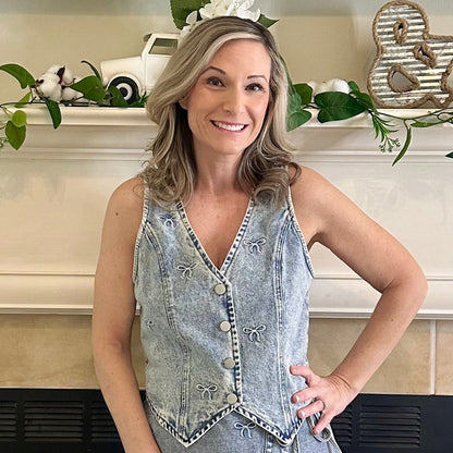 Woman in a denim dress and white boots standing in front of a fireplace.