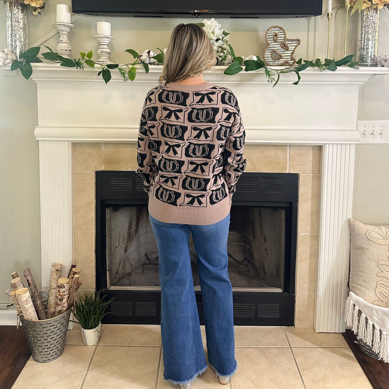 Person standing in front of a fireplace wearing a patterned sweater and blue jeans.