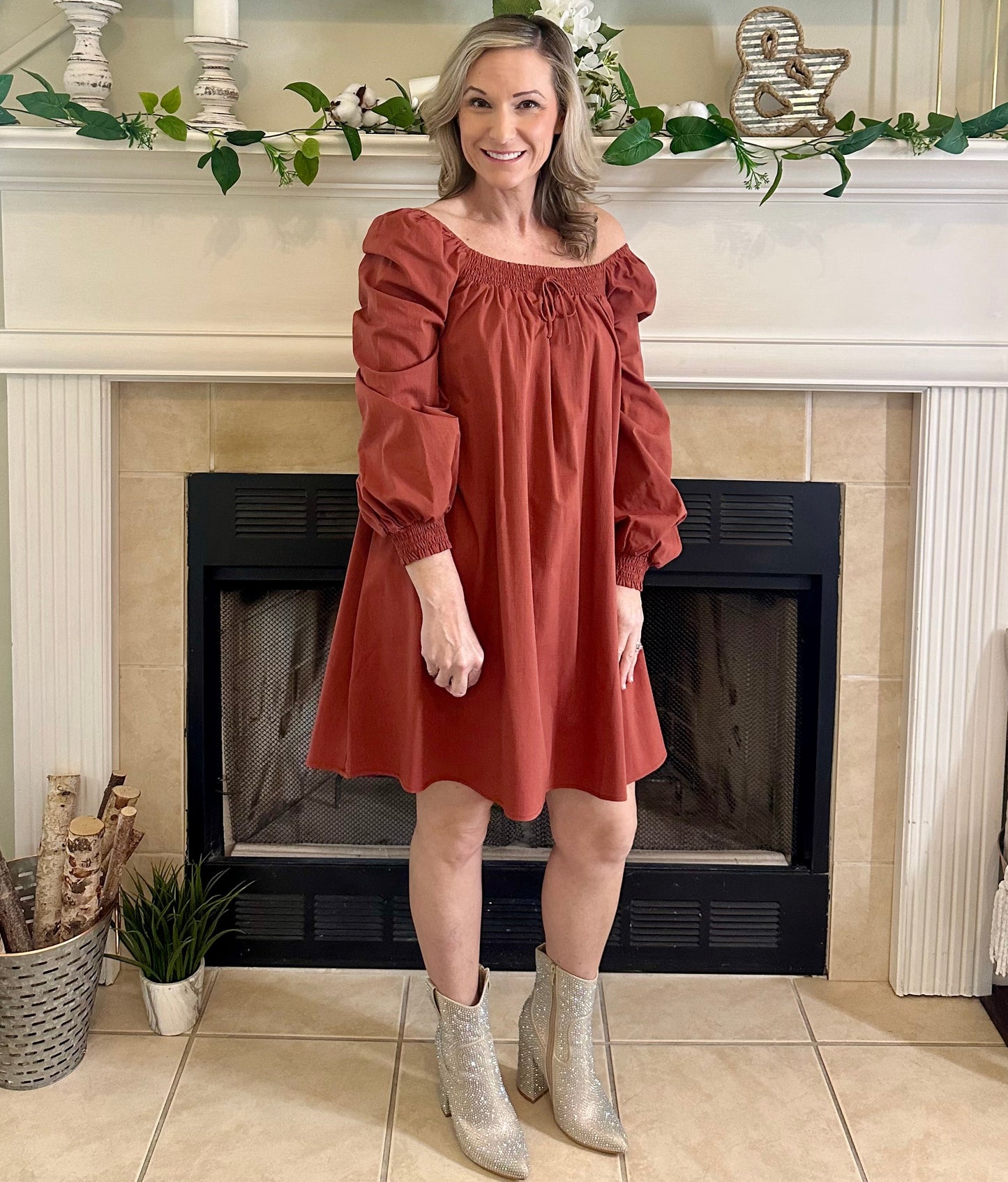 Woman in a rust color dress standing in front of a fireplace