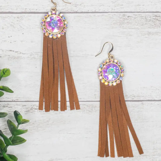 Brown tassel earrings with colorful gemstones on a white wooden surface.
